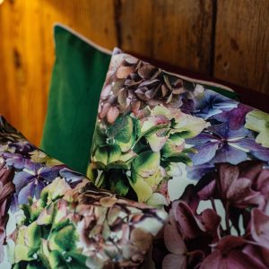 Coussin décoratif carré en velours, imprimé motif floral, dans des tons de roses, fushias, violet et verts sur fond écru