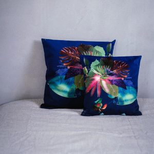 Coussin décoratif carré en velours, imprimé motif floral et végétal sur fond bleu, tons intenses de rose, vert, turquoise, violet